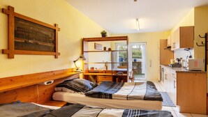 A compact room with two beds, a desk, a small kitchen area, and a view through a glass door. - Studio Apartment 'Gudrun' with Private Terrace, Shared Garden and Wi-Fi (Usingen)
