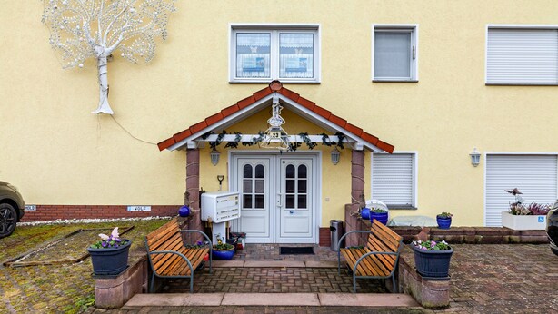 A building with a yellow facade, a white door with a red roof, and a tree sculpture on the wall. - Studio Apartment 'Gudrun' with Private Terrace, Shared Garden and Wi-Fi (Usingen)