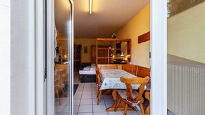 A dining area with a table and chairs, a wooden cabinet, and a sliding glass door leading to another room. - Studio Apartment 'Gudrun' with Private Terrace, Shared Garden and Wi-Fi (Usingen)