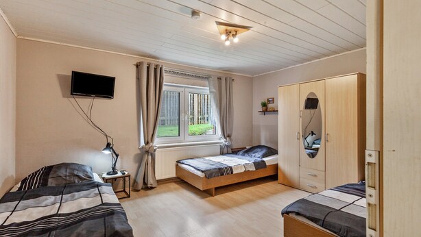 A bedroom with a bed, a bedside table, a lamp, a TV, a wardrobe, and a window. - Holiday Apartment 'Hildegard' with Shared Garden and Wi-Fi (Usingen)