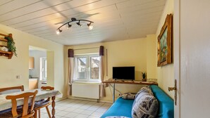 A room with a dining table, chairs, a sofa, a television, and a window with curtains. - Holiday Apartment 'Hildegard' with Shared Garden and Wi-Fi (Usingen)