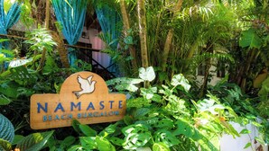 Une enseigne en bois portant l’inscription « NAMASTE BEACH BUNGALOW » et entourée d’une végétation luxuriante.