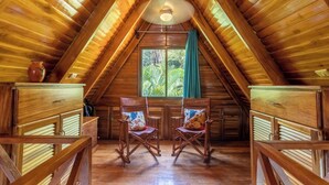Un intérieur en bois avec un plafond en pente, une fenêtre avec des rideaux et deux chaises en bois dotées de coussins.