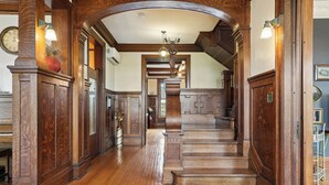 Eine imposante Holztreppe mit schwarzer Fußmatte am Fuß, die zu einer Empfangshalle im zweiten Obergeschoss führt.