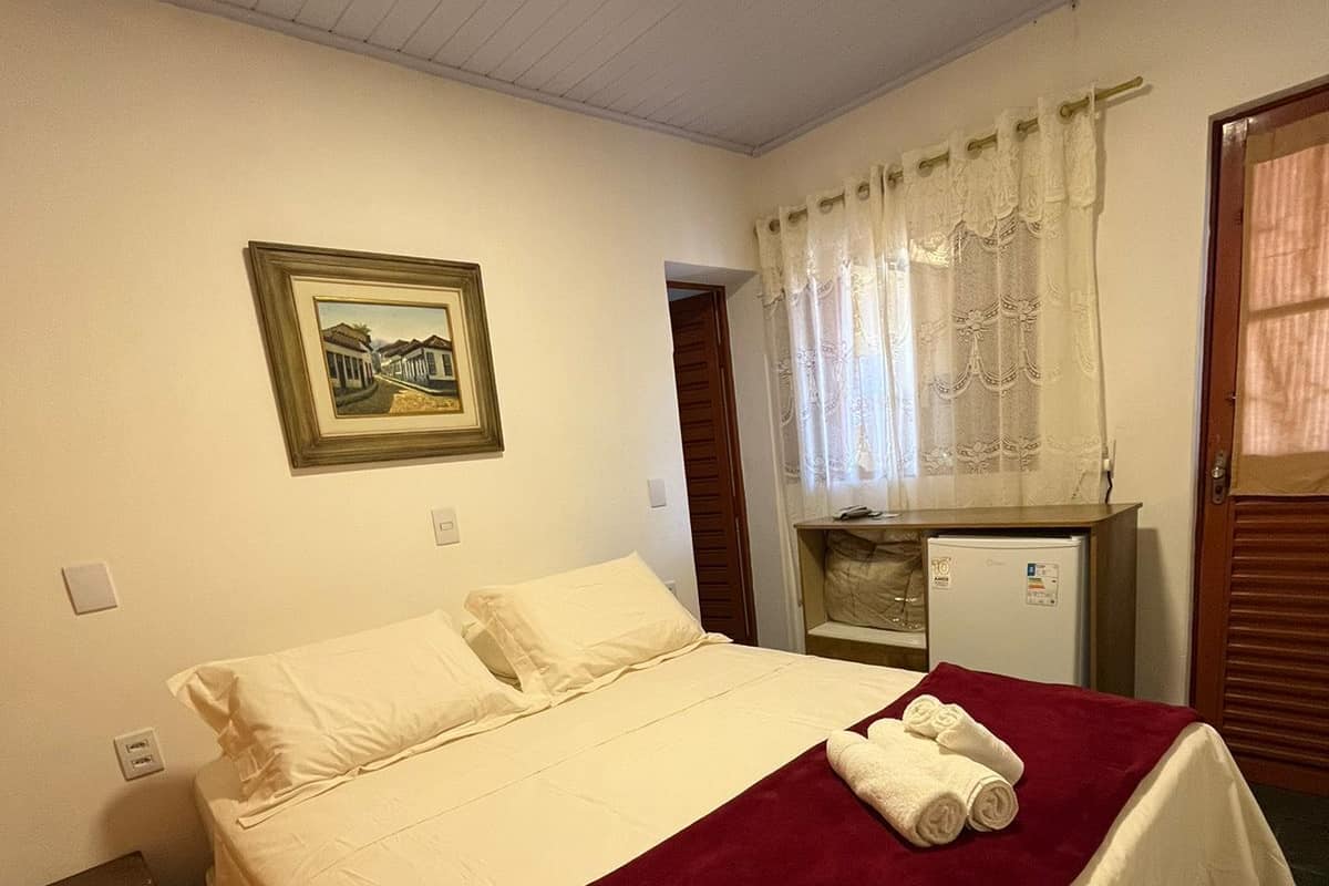 A hotel room with a bed, a desk, a refrigerator, and a framed picture on the wall.