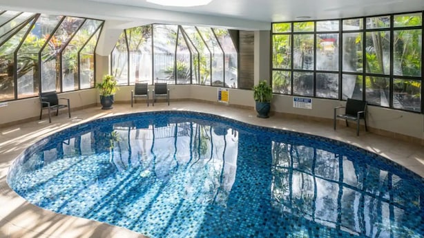 Una piscina interna con acqua cristallina e limpida, circondata da ampie vetrate che offrono vista sul verde.
