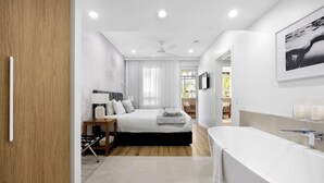 A modern bedroom with a large bed, a bedside table with a lamp, a ceiling fan, and a view of a balcony.