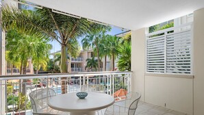 A balcony with a round table and chairs, overlooking a pool and palm trees.