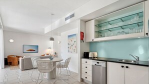A modern kitchen with a glass-fronted cabinet displaying glasses, a dishwasher, and a dining area with a round table and chairs.
