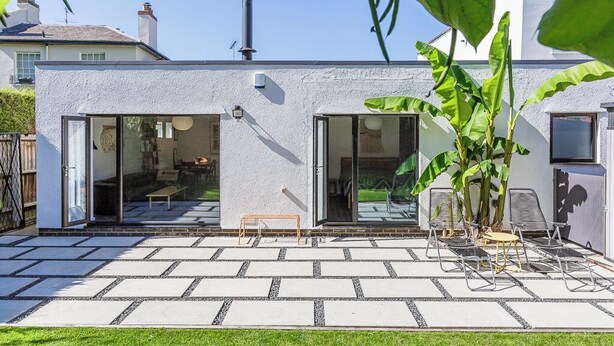 A modern house with a patio area featuring a seating arrangement and a large plant. - Mid-Century Modern Style 1BD with Garden (Cheltenham)