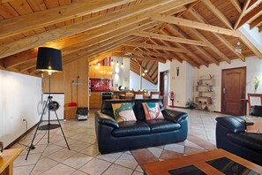 Un vaste espace de vie doté d’un haut plafond en bois, d’un canapé en cuir noir et d’un coin repas situé à l’arrière-plan.