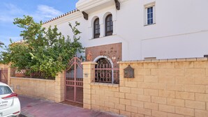 Valkoinen rakennus, jossa on portti, tiilimuuri ja puu sen edessä.