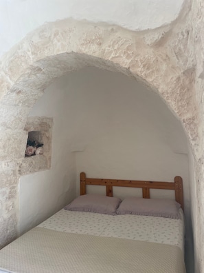 A bedroom with a stone arch, a wooden bed frame, and a small picture on the wall.