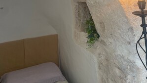 Une pièce avec une arche en pierre, un lit, une lampe fixée au mur et une petite plante.