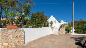 Un mur de pierre, un bâtiment blanc surmonté d’un toit conique et un escalier menant à l’étage supérieur.