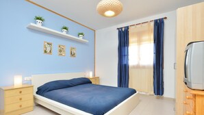 A bedroom with a bed, bedside tables, a shelf with plants, a TV, and a window with curtains. - Holiday Home 'Chalet Independiente Costa Daurada' with Private Garden, Balcony and Air Conditioning (Roda de Berà)
