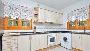 A kitchen with wooden cabinets, a washing machine, and a window with lace curtains. - Holiday Home 'Chalet Independiente Costa Daurada' with Private Garden, Balcony and Air Conditioning (Roda de Berà)