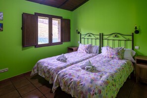 Une chambre avec deux lits, des murs verts, une fenêtre avec des volets en bois et une tête de lit en métal.