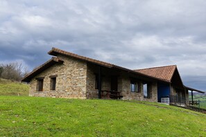 Un bâtiment en pierre avec un toit en pente, un porche et une colline verdoyante au premier plan.