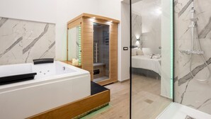 Un baño moderno con una bañera grande, una ducha con paredes de vidrio y una habitación visible con una cama.