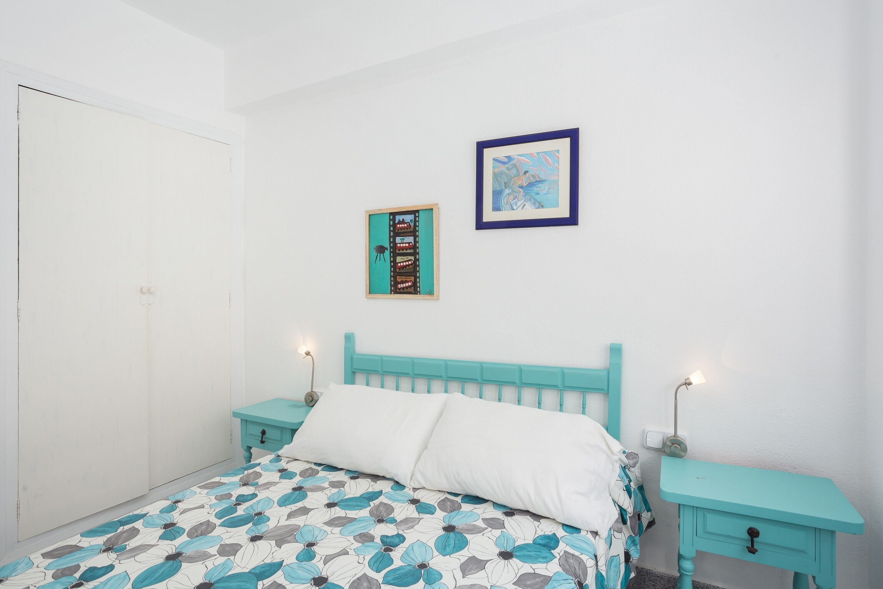 Une chambre à coucher comprenant un lit, deux tables de chevet, une armoire et deux tableaux encadrés accrochés au mur.