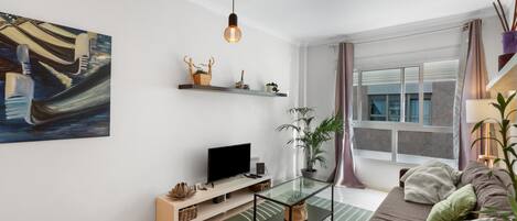 A modern living room with a flat-screen TV, a glass coffee table, a sofa, a large abstract painting, and a window with curtains.