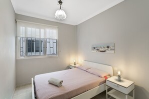 A bedroom with a bed, bedside tables, a window, and a hanging light fixture.