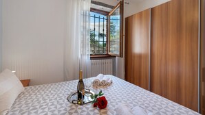 Ein Hotelzimmer mit einem Bett, einem Vorhangfenster, einem Holzschrank und einem Tablett mit einer Flasche und Gläsern.