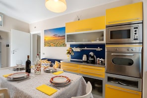 A modern kitchen with yellow cabinets, a built-in oven, and a dining area set with plates, glasses, and a bottle. - Apartment 'Res Jasmine- Appartamento Yellow' with Mountain View, Shared Garden and Wi-Fi (Verbania)