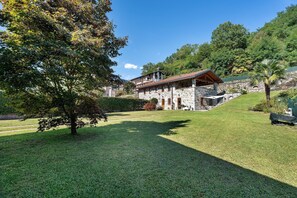 A stone building with a balcony, surrounded by a well-maintained lawn and trees. - Apartment 'Res Jasmine- Appartamento Yellow' with Mountain View, Shared Garden and Wi-Fi (Verbania)