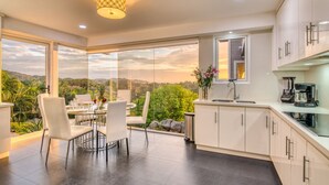 Une cuisine moderne dotée d’une grande fenêtre donnant sur un paysage magnifique, un coin repas avec une table et des chaises, et une machine à café posée sur le plan de travail.