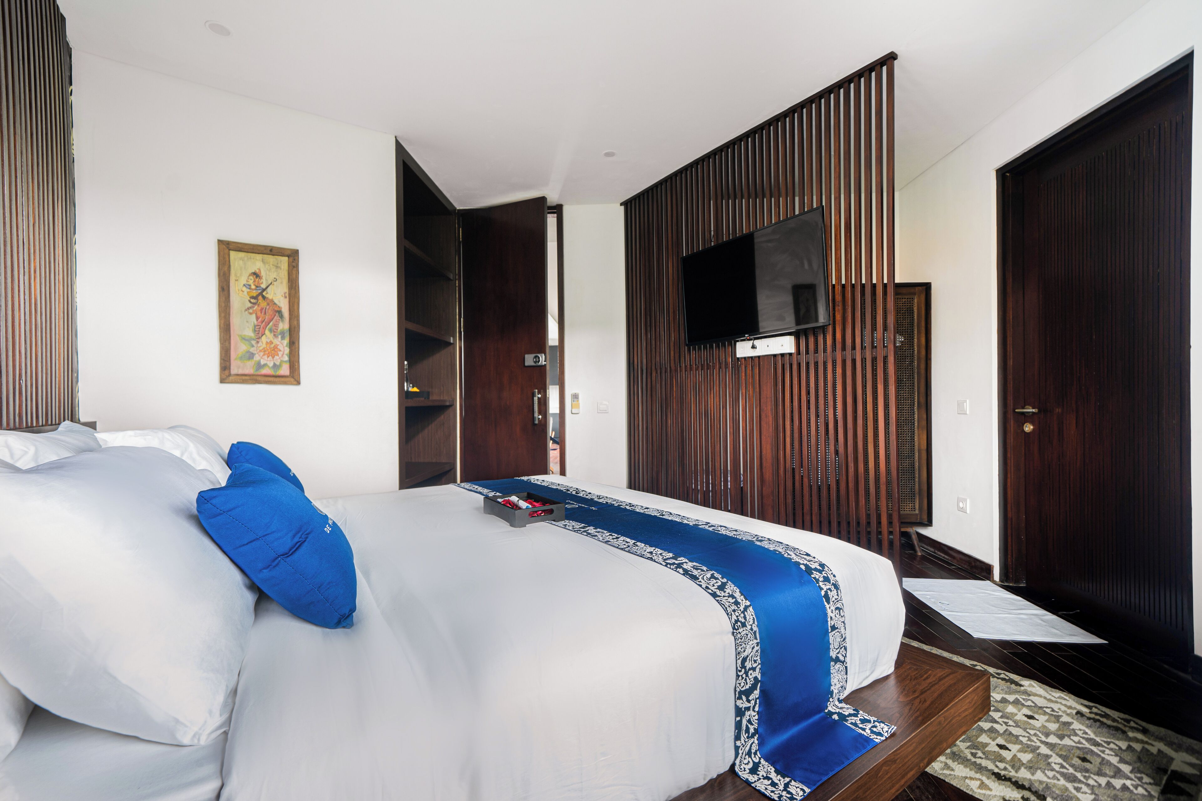 A hotel room with a large bed, a flat-screen TV mounted on a wooden panel, and a door leading to another room.