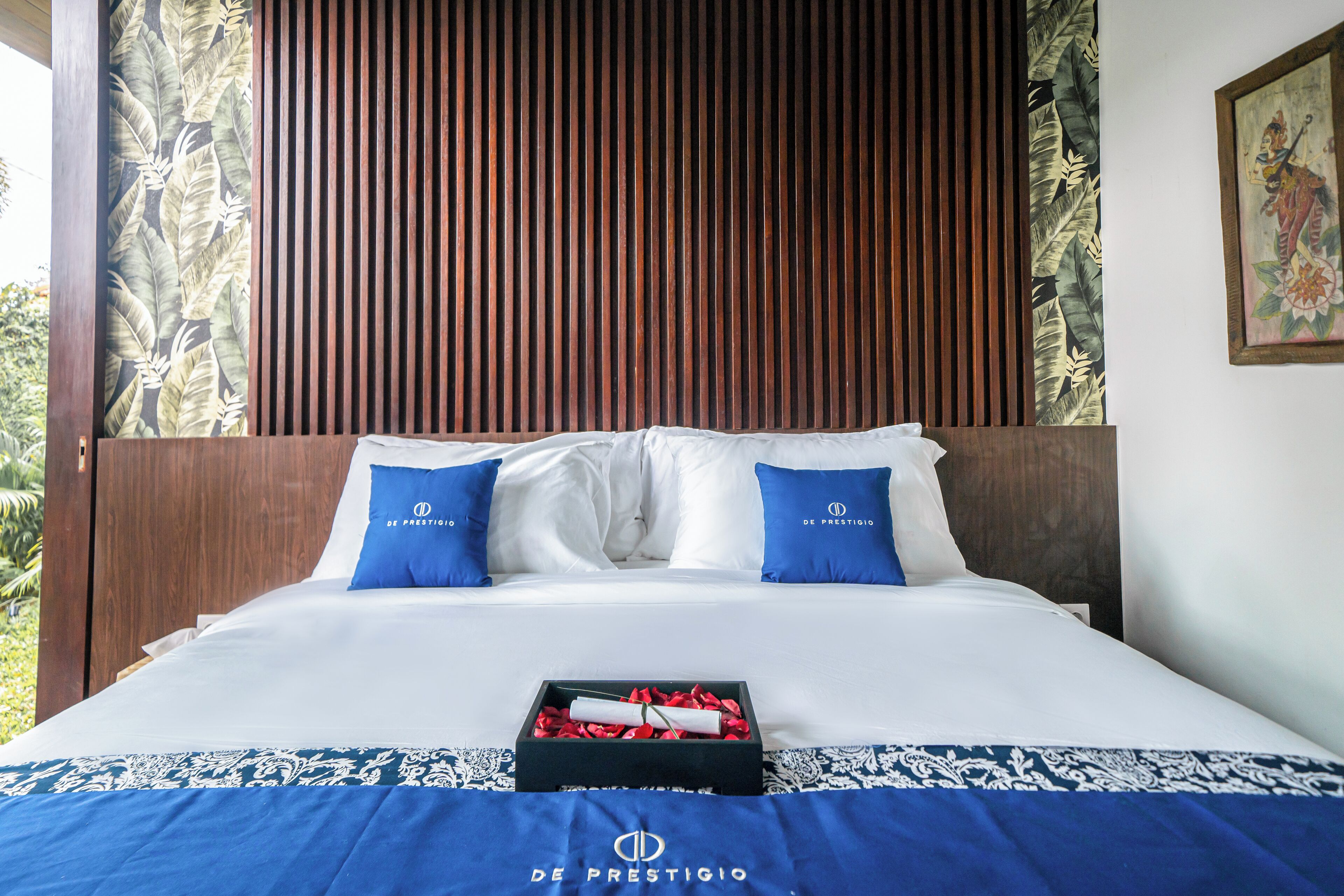 Habitación de hotel con una cama, ropa de cama blanca y azul, un cabecero de madera y una manta azul con un logotipo.