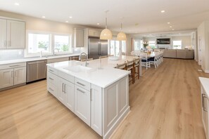 A modern kitchen with white cabinetry, a large island, pendant lighting, and a dining area with a sofa.