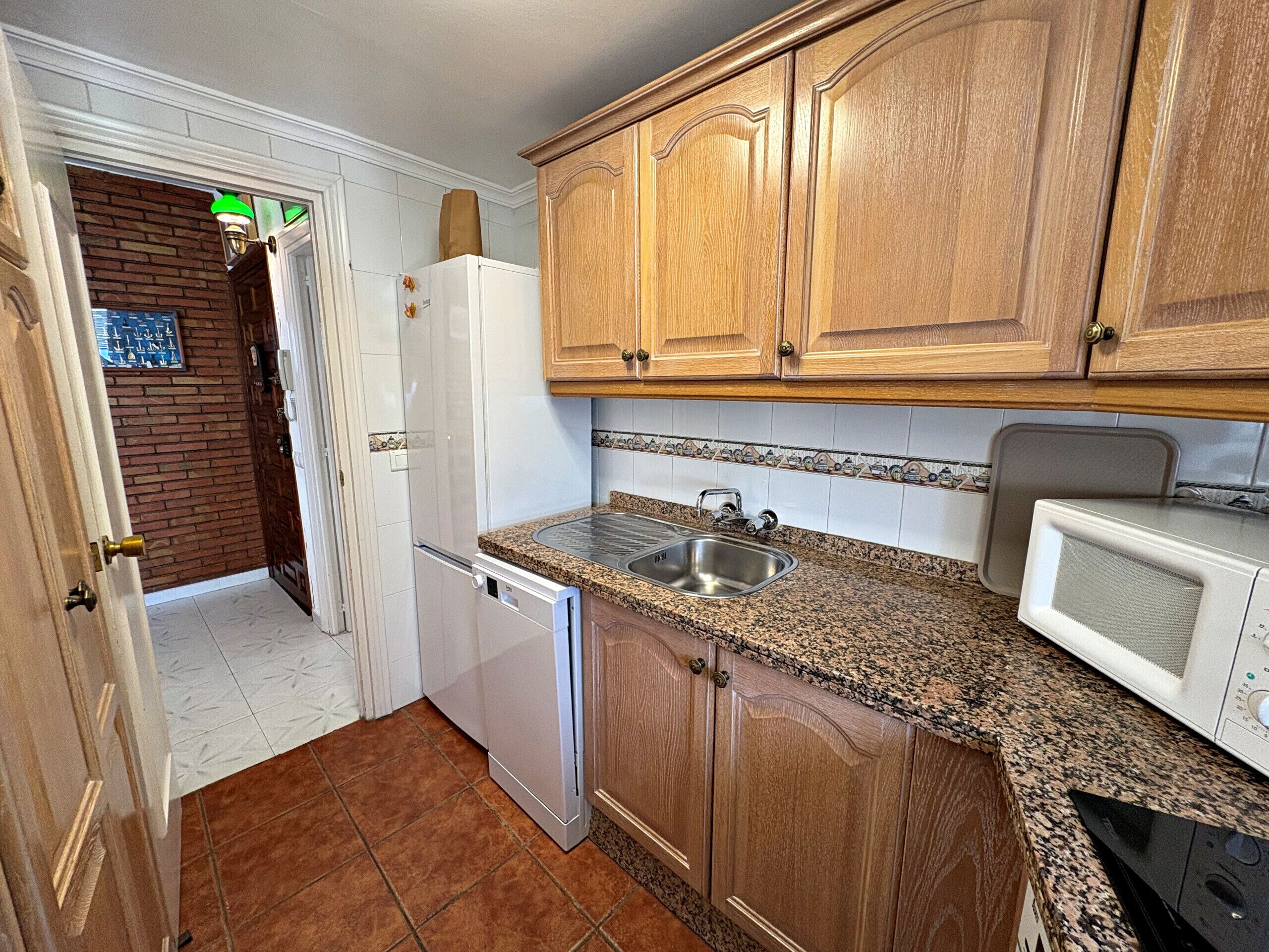 A kitchen with wooden cabinets, a white refrigerator, a microwave, and a sink.