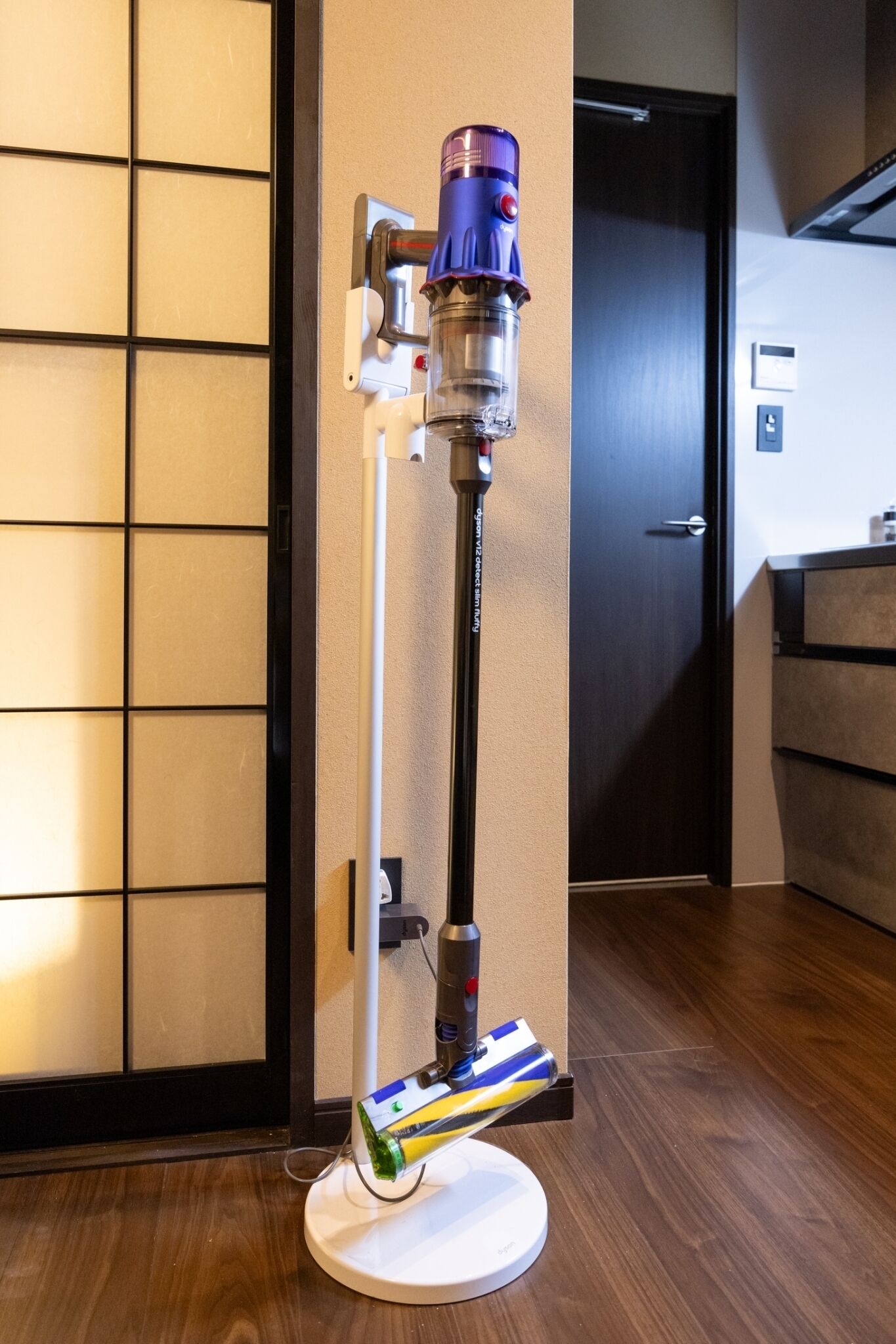 A room with a door, a wall-mounted light fixture, and a wooden floor.