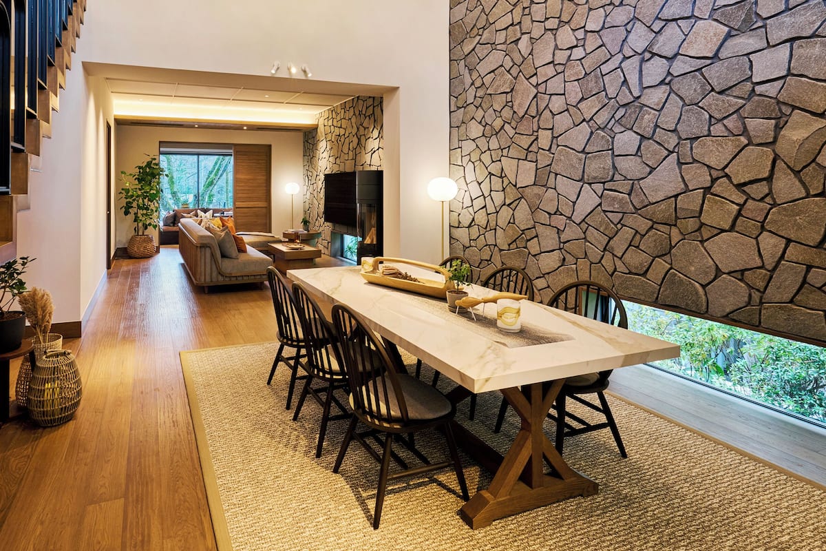 A spacious dining area with a long table, chairs, and a stone wall.