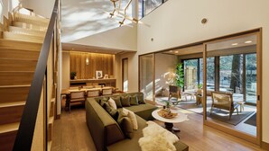 A modern interior with a staircase, a green sofa, a dining area, and large windows offering a view of the outdoors. - GLAMDAY STYLE HOTEL SUITE KAWANONE (Karuizawa)