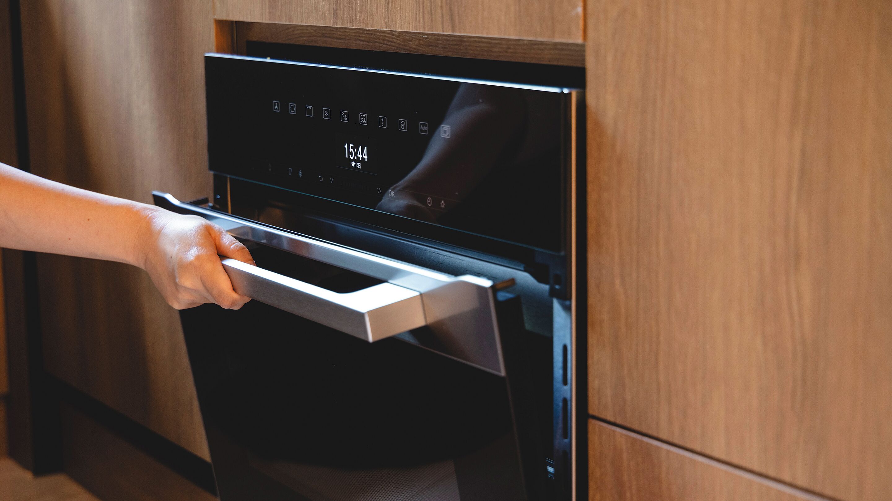 Une main ouvrant la porte d’un four moderne doté d’un écran numérique.