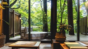 Una habitación con vistas a un bosque verde exuberante a través de amplios ventanales, un banco de madera, una pequeña mesa y una planta en maceta.