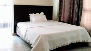 A neatly made bed with white bedding in a room with light-colored walls and a dark headboard. - Kigali view Garden apart (Kigali)