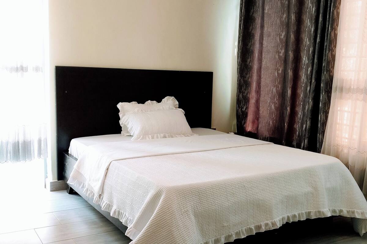 A neatly made bed with white bedding in a room with light-colored walls and a dark headboard.