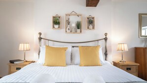 A neatly made bed with a wooden headboard, two bedside tables with lamps, and three wall-mounted plant frames. - Maple Cottage - Beautiful 2BD Retreat (Chipping Norton)