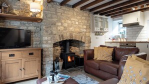 A cozy living room with a stone fireplace, a television, and a leather sofa. - Maple Cottage - Beautiful 2BD Retreat (Chipping Norton)