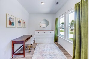 A room with a desk, a dresser, a mirror, and a window with curtains.