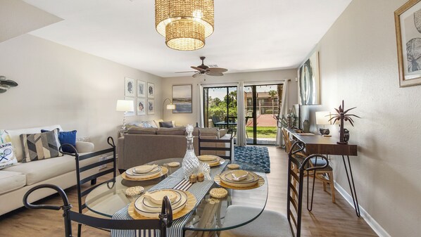 A dining area with a glass table, chairs, and a ceiling fan.