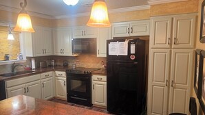 Una cocina con armarios blancos, un refrigerador negro, una estufa y un microondas.