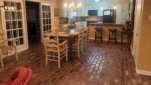 Una cocina amplia con comedor, que cuenta con piso de ladrillo, sillas de madera y una isla central con taburetes.