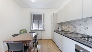 Una cocina compacta con una mesa de comedor de madera, dos sillas, un ventanal con persianas y un salpicadero de azulejos.