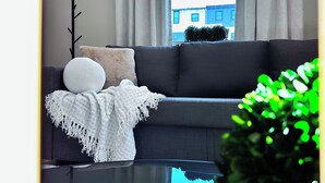 A modern living room with a grey sofa, a white throw blanket, and a white cushion.